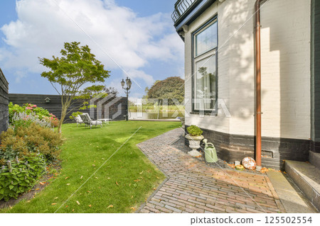 A serene garden featuring lush greenery and a charming brick pathway beside a contemporary home, perfect for outdoor relaxation and landscaping inspiration. A serene garden featuring lush greenery and a charming brick pathway beside a contemporary home, perfect for outdoor relaxation and landscaping inspiration. 125502554