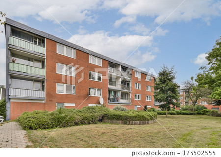 A contemporary-style apartment building with balconies surrounded by lush greenery and trees, reflecting a harmonious blend of architecture and nature. A contemporary-style apartment building with balconies surrounded by lush greenery and trees, reflecting a harmonious blend of architecture and nature. 125502555