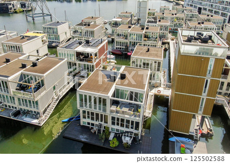Aerial view of contemporary floating houses arranged near a canal, showcasing innovative architecture and vibrant colors in urban living. 125502588