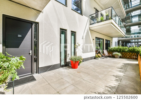 This image showcases a stylish modern apartment entrance surrounded by vibrant greenery and sleek architectural design elements. 125502600