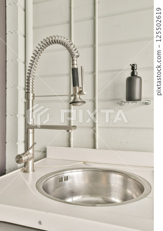 A sleek, modern kitchen sink features a stainless steel basin and an elegant pulldown faucet. This design combines functionality with contemporary aesthetics. 125502619