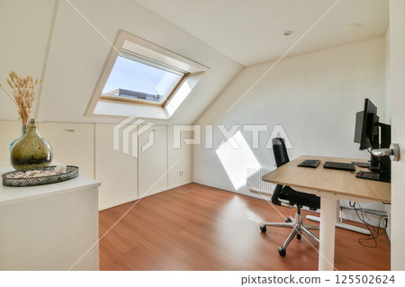 A bright and airy modern home office featuring a sleek desk, ergonomic chair, and decorative vase, ideal for productivity and comfort. 125502624