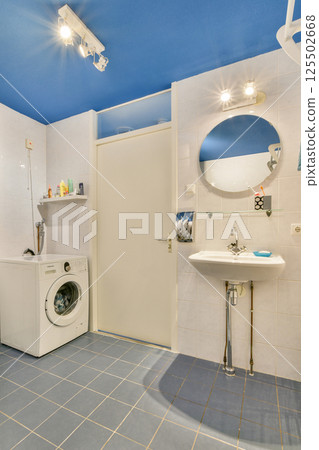 A contemporary laundry room featuring a washing machine, a round mirror, and a bright blue ceiling, designed for functionality and style. A contemporary laundry room featuring a washing machine, a round mirror, and a bright blue ceiling, designed for functionality and style. 125502668