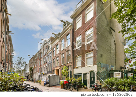 A picturesque view of a street in Amsterdam, featuring charming buildings, lush trees, and bicycles parked along the path, capturing the essence of Dutch architecture. 125502802