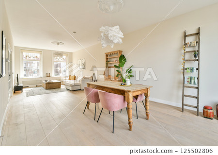 A beautifully designed modern living room featuring minimalistic decor, a wooden table, stylish seating, and warm lighting enhancing the inviting atmosphere. 125502806