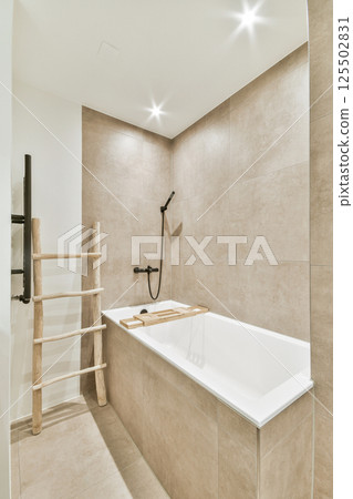 A sleek and modern bathroom featuring a bathtub, wooden ladder, and neutral tones that create a calming atmosphere. 125502831