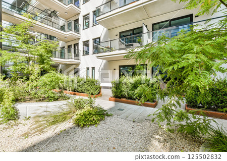 Contemporary building design featuring spacious balconies surrounded by vibrant plants and well-maintained landscaping, creating a serene urban environment. 125502832