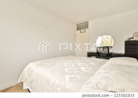 A spacious modern bedroom featuring a light color palette, elegant decor, and minimalistic furniture that enhances the room's tranquility. 125502835