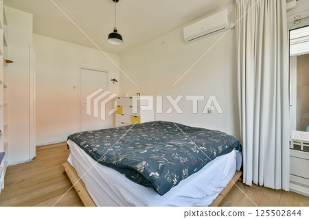 A serene modern bedroom featuring a comfortable bed, soft linens, and minimalistic decor, complemented by natural light from a window. 125502844