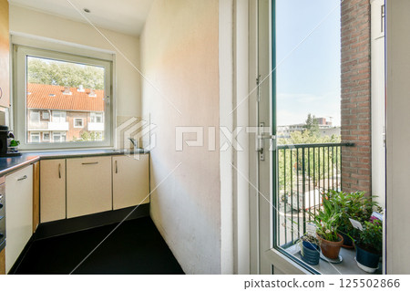 Bright and airy kitchen featuring a window view of a balcony with potted plants, sunlight streaming in, enhancing the modern aesthetic of the space. 125502866