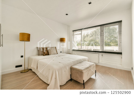 A sleek, minimalist bedroom featuring contemporary furniture, warm lighting, and large windows allowing natural light to fill the space. 125502900