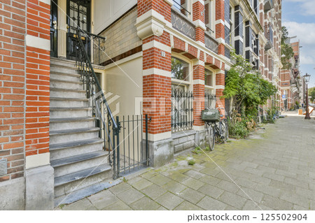A picturesque view showcasing a charming brick building's entrance with well-designed stairs, a bicycle, and greenery lining the pathway. Ideal for urban architecture lovers. 125502904