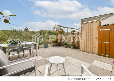 A beautifully arranged outdoor patio featuring comfortable seating, potted plants, and a rustic wooden fence, perfect for relaxation and gatherings. 125502963
