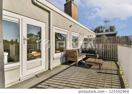 A stylish modern terrace featuring comfortable seating, wooden details, and an inviting atmosphere under a clear blue sky, perfect for relaxation. 125502969