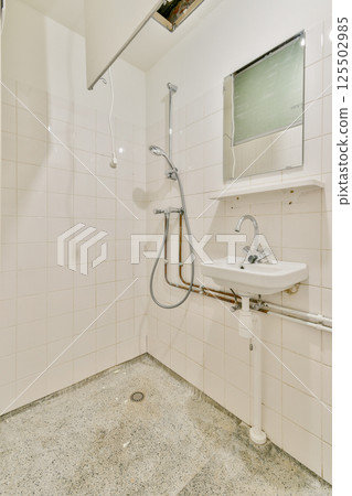 A clean and contemporary bathroom featuring a shower fixture and minimalist design. The tiles and faucet create a refreshing atmosphere suitable for relaxation. 125502985