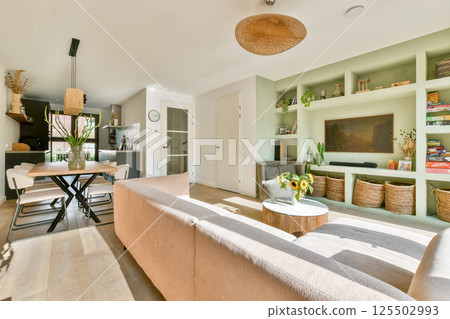 A spacious and inviting modern living room seamlessly connected to a dining area, featuring elegant furniture and natural light. 125502993