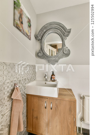 A contemporary bathroom featuring a sleek wooden cabinet and a decorative mirror. The design is minimalistic, combining functionality with elegance. 125502994