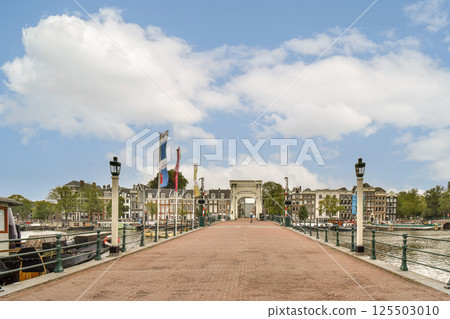 A picturesque view of a waterfront pathway leading towards historic buildings under a vibrant sky, capturing the charm of Amsterdam's architecture. A picturesque view of a waterfront pathway leading towards historic buildings under a vibrant sky, capturing the charm of Amsterdam's architecture. 125503010