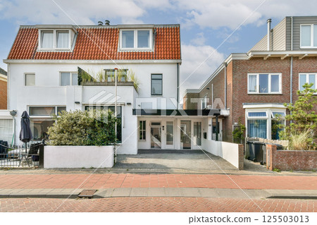 View of modern residential buildings with distinct architectural designs, featuring red roofs and greenery, set against a clear sky. View of modern residential buildings with distinct architectural designs, featuring red roofs and greenery, set against a clear sky. 125503013