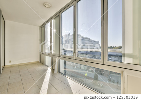 A bright and airy interior featuring large glass windows providing natural light, showcasing a minimalistic design with tiled flooring and a spacious feel. A bright and airy interior featuring large glass windows providing natural light, showcasing a minimalistic design with tiled flooring and a spacious feel. 125503019