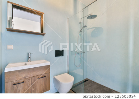 A sleek modern bathroom featuring a glass shower, minimalist sink, and contemporary decor with cool blue walls. A sleek modern bathroom featuring a glass shower, minimalist sink, and contemporary decor with cool blue walls. 125503054
