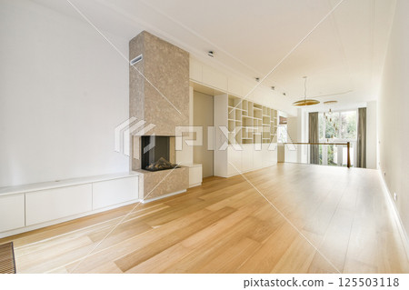 A spacious, minimalist interior featuring a light wooden floor, elegant decor, and a stylish fireplace. The room exudes tranquility and modernity. 125503118
