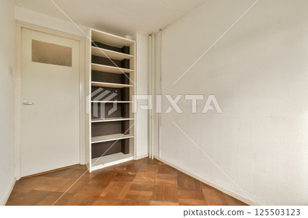 A simple interior space featuring a light-colored wall, wooden flooring, and a narrow shelf against the wall, creating a clean and uncluttered appearance. A simple interior space featuring a light-colored wall, wooden flooring, and a narrow shelf against the wall, creating a clean and uncluttered appearance. 125503123