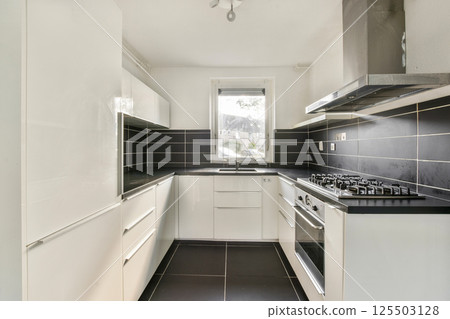 This kitchen features a sleek design with white cabinetry, black countertops, and modern appliances, emphasizing functionality and style in a compact space. This kitchen features a sleek design with white cabinetry, black countertops, and modern appliances, emphasizing functionality and style in a compact space. 125503128