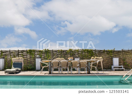 A stylish outdoor patio featuring a swimming pool, wooden fencing, and comfortable seating arrangements under a clear blue sky, perfect for relaxation. A stylish outdoor patio featuring a swimming pool, wooden fencing, and comfortable seating arrangements under a clear blue sky, perfect for relaxation. 125503141