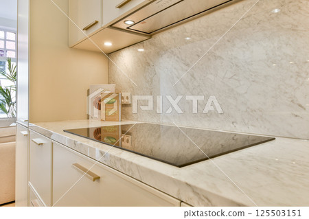 A beautifully designed modern kitchen featuring sleek marble countertops, contemporary cabinetry, and a spacious layout filled with natural light. 125503151