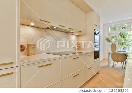 A sleek and stylish modern kitchen featuring beige cabinets, marble countertops, and contemporary lighting creating an inviting atmosphere for cooking and dining. 125503201