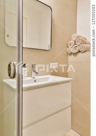 Elegant bathroom featuring contemporary tiles, a stylish sink, and plush towels. A serene atmosphere is created with clean lines and neutral colors. Elegant bathroom featuring contemporary tiles, a stylish sink, and plush towels. A serene atmosphere is created with clean lines and neutral colors. 125503203
