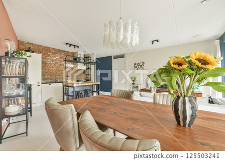 A stylish dining area featuring a wooden table, elegant chairs, and vibrant sunflowers in a vase, complemented by contemporary decor and a cozy atmosphere. A stylish dining area featuring a wooden table, elegant chairs, and vibrant sunflowers in a vase, complemented by contemporary decor and a cozy atmosphere. 125503241