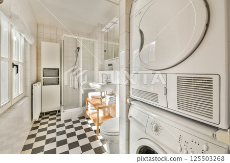 A stylish bathroom featuring modern laundry appliances alongside sleek fixtures, clean lines, and a checkered floor design that enhances the overall aesthetic. 125503268