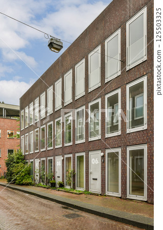 A contemporary residential structure featuring multiple windows and a blend of brick and glass materials, set against a cloudy sky. A contemporary residential structure featuring multiple windows and a blend of brick and glass materials, set against a cloudy sky. 125503325