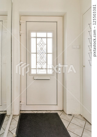 A sleek modern entrance door featuring a glass panel design, accompanied by a large mirror and elegant tile flooring, creating a welcoming ambiance. 125503381