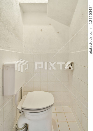 A well-maintained bathroom showing a white ceramic toilet and tiled walls, emphasizing cleanliness and minimalism in design. 125503424
