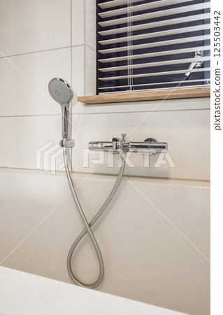 A sleek and contemporary shower fixture stands out against a clean tiled wall, featuring minimalistic design and elegant chrome detailing. 125503442