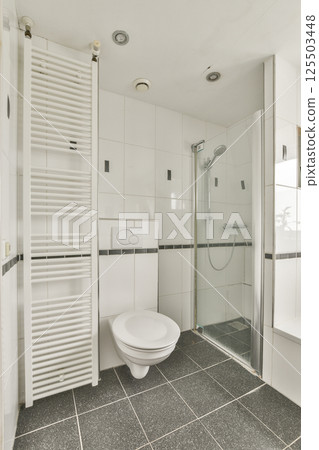 A spacious and elegant bathroom showcasing sleek tiles, a modern shower setup, and a stylish wall radiator for comfort and aesthetics. 125503448