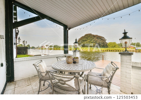 A charming outdoor patio featuring a round table and chairs, surrounded by greenery and looking out over calm waters, creating a perfect relaxation spot. 125503453
