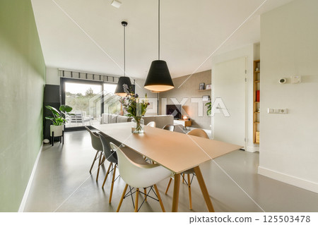 A stylish dining room featuring a minimalist design, a large table surrounded by chairs, and a green accent wall. Natural light enhances the contemporary decor. A stylish dining room featuring a minimalist design, a large table surrounded by chairs, and a green accent wall. Natural light enhances the contemporary decor. 125503478