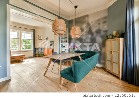 A stylish living room featuring a wooden table, teal chairs, and unique lighting. Fresh flowers add a touch of nature to the contemporary space. A stylish living room featuring a wooden table, teal chairs, and unique lighting. Fresh flowers add a touch of nature to the contemporary space. 125503515