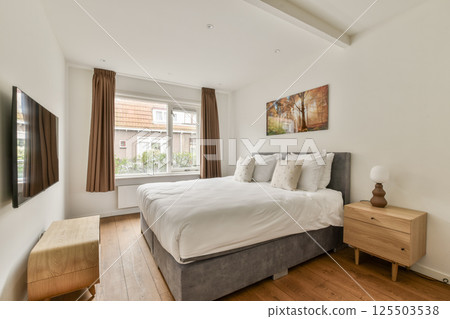 A sleek, modern bedroom featuring a cozy bed, soft textiles, and elegant decor. Natural light spills in from the window, enhancing the serene ambiance. 125503538