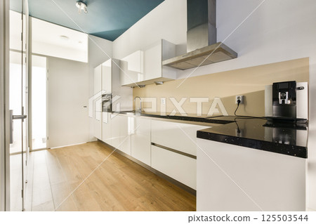 A sleek, modern kitchen featuring white cabinetry, a black countertop, and clean lines. The design emphasizes simplicity and functionality in the space. 125503544