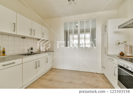 A bright and modern minimalist kitchen featuring sleek cabinets, a stylish stove, and large windows for natural light. A bright and modern minimalist kitchen featuring sleek cabinets, a stylish stove, and large windows for natural light. 125503556