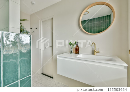 A stylish bathroom featuring green tiles, a circular mirror, and a white wall-mounted sink, creating a sleek and contemporary ambiance. A stylish bathroom featuring green tiles, a circular mirror, and a white wall-mounted sink, creating a sleek and contemporary ambiance. 125503634