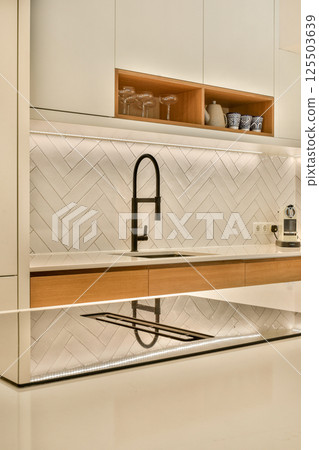 A sleek modern kitchen featuring a herringbone patterned backsplash and minimalist fixtures. The design emphasizes elegance and functionality. 125503639