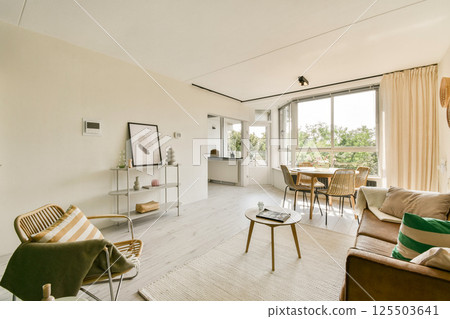 A spacious and contemporary living area featuring large windows, stylish furniture, and minimalistic decor, creating an inviting atmosphere with natural light. 125503641