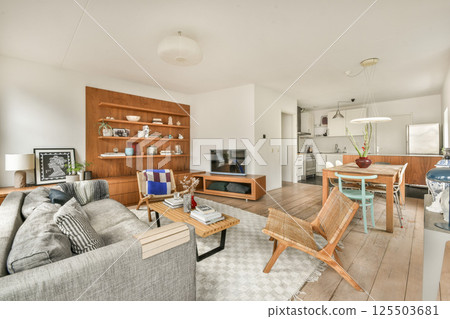 A stylish modern living room featuring a cozy sofa and adjacent dining area. The space showcases minimalist decor with warm wood accents and ample natural light. A stylish modern living room featuring a cozy sofa and adjacent dining area. The space showcases minimalist decor with warm wood accents and ample natural light. 125503681