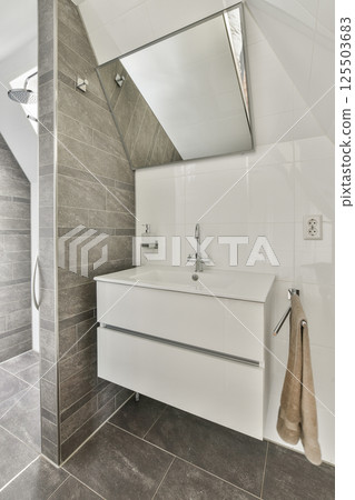 A sleek and contemporary bathroom featuring gray tiles, a stylish white vanity, and a large mirror that enhances the space's aesthetic balance. 125503683